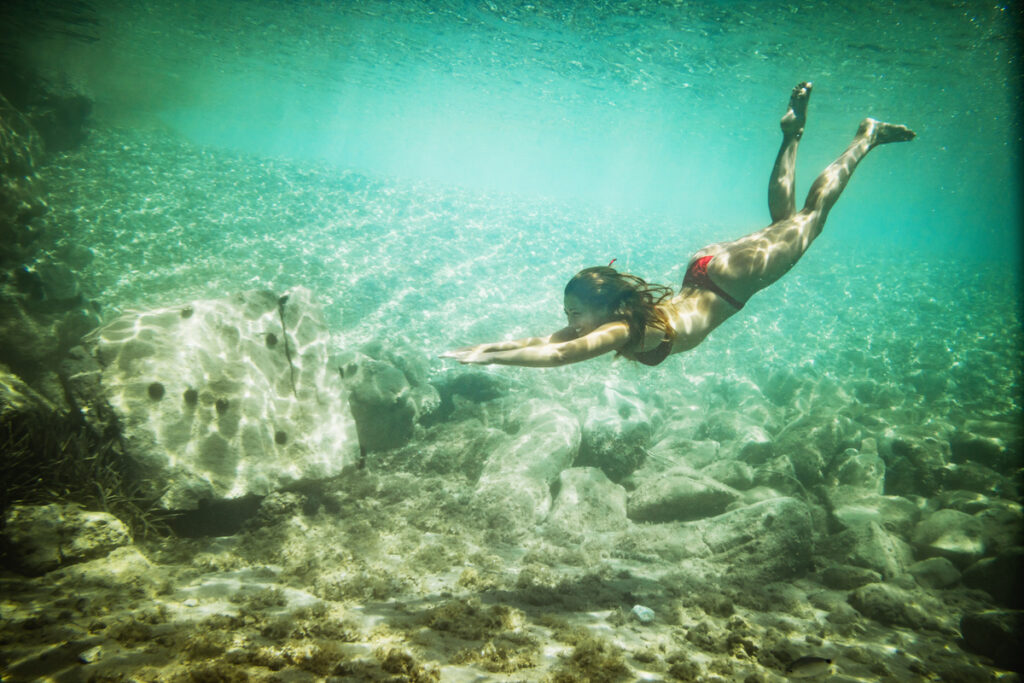 A beautiful young woman is having fun on summer vacation exploring the seafloor during freediving in the sea.